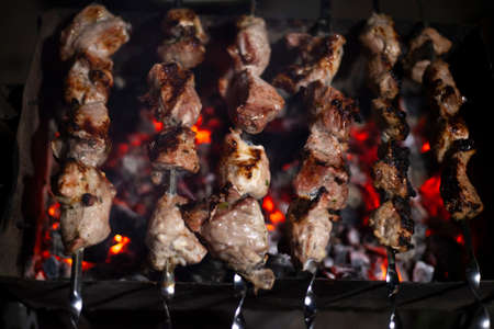 The meat is fried over an open fire. Skewers set on skewers are cooked on a mongal. National cuisine of the Caucasian peoples. Delicious meat gives juice from high temperature. Cooking at night on the street.の写真素材