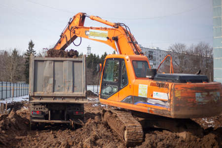 A machine at a construction site digs the ground. An escalator is preparing a construction site. Building a house. The work of heavy equipment. Preparation of the foundation of the house. Construction of a residential complex.の写真素材