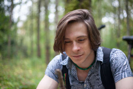 Portrait of a young man in a park. The guy is looking at the camera. Walk in nature. A man in a shirt and with long hair.の写真素材