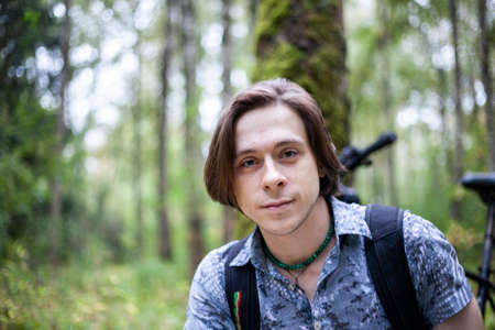 Portrait of a young man in a park. The guy is looking at the camera. Walk in nature. A man in a shirt and with long hair.の写真素材