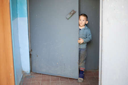 The boy opens the door to the entrance to the apartment building. The child ran away from the apartment. The preschooler went for a walk. The kid hardly opens the door. High location of the door handle for a small person.の写真素材