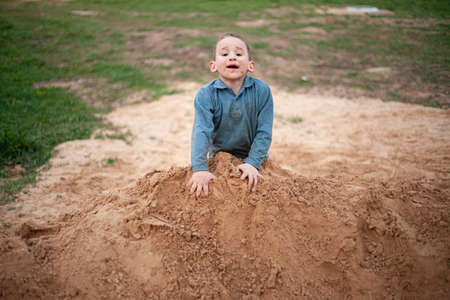 A child plays in a pile of dog. The boy has fun in the playground. A hyperactive child is wallowing in the sand. Children's joy in life. Fun activity for the child. Son spends energy on the game.の写真素材