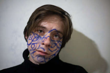 A guy with a pattern on his face. Creative person. The artist expresses himself. The poet portrayed his thoughts on his face. Painted body. Young joker. At the party. Funny friends.の写真素材