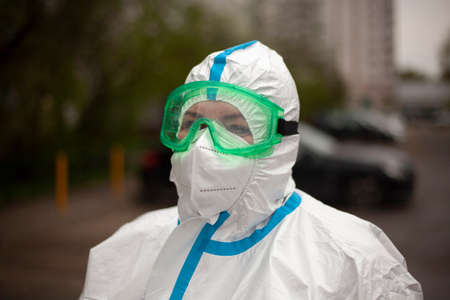 A doctor in a protective suit on the street. Infectionist in a mask and glasses. A paramedic came to do a coronavirus test in sheltered clothing. Portrait of a nurse during a global epidemic.の写真素材