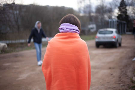 A blanket on the shoulders of a girl. The woman froze and covered herself with a warm blanket. The girl looks at a car leaving in the distance. The state of human expectation.の写真素材