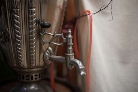 Russian samovar for tea drinking. Vintage kettle for hot water. The tradition of drinking a hot drink with sweets. Polished steel metal item.の写真素材