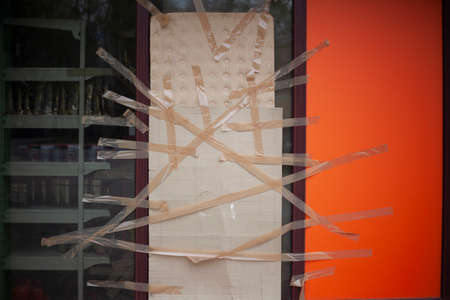 Broken shop window taped with tape and cardboard. An act of vandalism on the street. A randomly broken window. Homemade repairs on their own.の写真素材