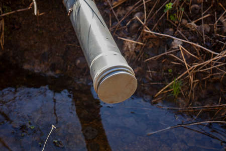 Pipe for draining water from a gutter. A device for regulating the liquid level in the channel. A plastic pipe sticks out of the ground. Pumping precipitation from the ditch.の写真素材