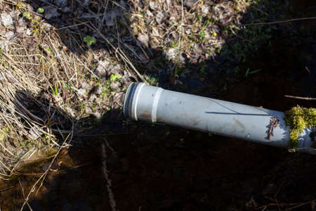 Pipe for draining water from a gutter. A device for regulating the liquid level in the channel. A plastic pipe sticks out of the ground. Pumping precipitation from the ditch.の写真素材
