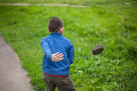The child throws a stone. The boy took the cobblestone in his hands. Renok is showing aggression. A splash of strength in a younger student. The boy throws a piece of asphalt. A homeless child throws out a heavy object.の写真素材