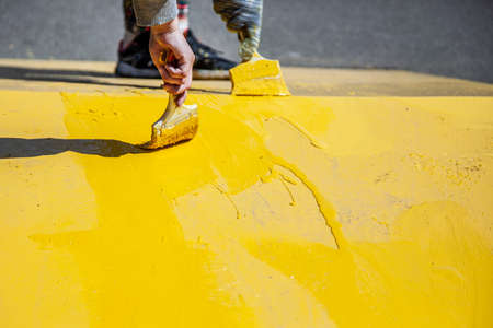Painting objects in the park in yellow. Yellow oil paint. Work of the park improvement worker. Brush with yellow paint on a pile. Drawing a thick layer of paint on the surface.の写真素材