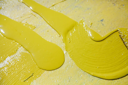 Painting objects in the park in yellow. Yellow oil paint. Work of the park improvement worker. Brush with yellow paint on a pile. Drawing a thick layer of paint on the surface.の写真素材
