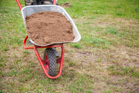 The gardener sprinkles a flower bed with a shovel. Creation of landscape design in the garden. The man is working. Gardening with a ground and a spade are tools of a gardener. A loose flower bed for flowers. Park decoration.の写真素材