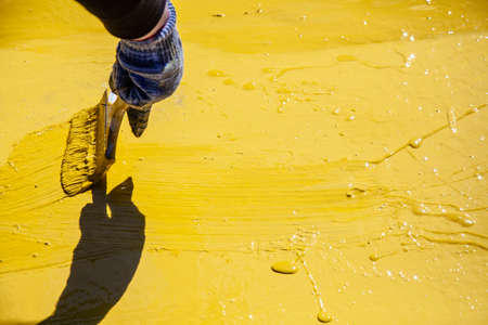 Painting objects in the park in yellow. Yellow oil paint. Work of the park improvement worker. Brush with yellow paint on a pile. Drawing a thick layer of paint on the surface.の写真素材