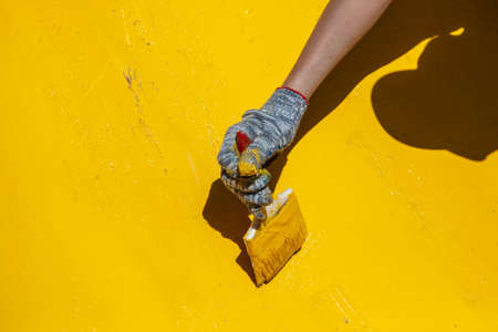 Painting objects in the park in yellow. Yellow oil paint. Work of the park improvement worker. Brush with yellow paint on a pile. Drawing a thick layer of paint on the surface.の写真素材
