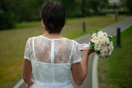 Bride with a bouquet in her hands. A girl in a white dress with a bouquet of roses is photographed from the back. The bride prepares to throw the bouquet.の写真素材