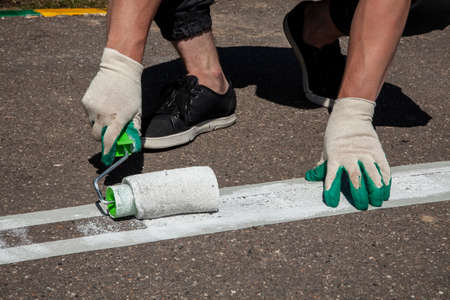 The roller with paint. Painting the bike path. Drawing a marking line in the Park. White stripe on the asphalt.の写真素材