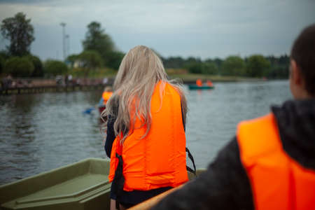 Girl in a life jacket on a boat. Water recreation. Boat trip on the city lake. Orange swimming vest for a woman.の写真素材