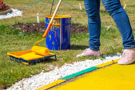 Painting objects in the park in yellow. Yellow oil paint. Work of the park improvement worker. Brush with yellow paint on a pile. Drawing a thick layer of paint on the surface.の写真素材
