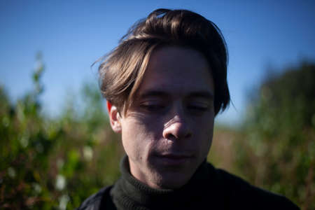 Portrait of a guy. Man's face on a background of blue sky. Walk in nature. Short-haired guy. Summer morning.の写真素材