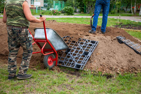 The gardener sprinkles a flower bed with a shovel. Creation of landscape design in the garden. The man is working. Gardening with a ground and a spade are tools of a gardener. A loose flower bed for flowers. Park decoration.の写真素材