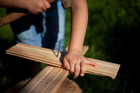 Child girl hammers a nail into the board. Playing with a hammer. Children's hobby in the father's workshop.の写真素材