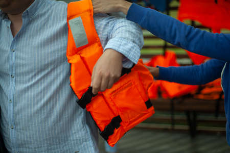 Puts on a life jacket. A man prepares to swim on the lake. Compliance with safety measures on the water. Life preserving orange vest.の写真素材