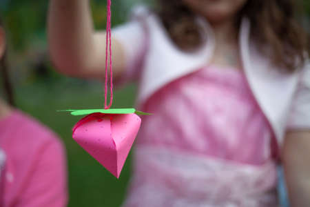 Children's hobby paper toys. Paper strawberries on a rope. The girl holds her creative work by the thread. Handicraft classes with children.の写真素材