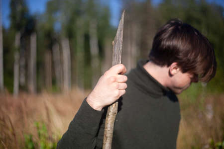 Guy with a stick in nature. A young man stands with a wooden pole. A man walks in the field. Rest away from the city.の写真素材