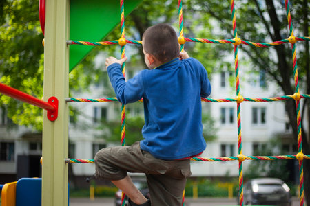 The child is climbing the net. Boy in the playground. Walk with my son in the street. The child...