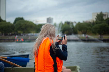 Life jacket on the girl. Orange life jacket on a woman sailing in a boat. Girl with phones in hands on the water.の写真素材