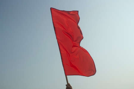 Red flag against the sky. Flag to signal the start of the competition. The symbol of the communist struggle. Red canvas on the staff. Matter vibrates in the wind.の写真素材