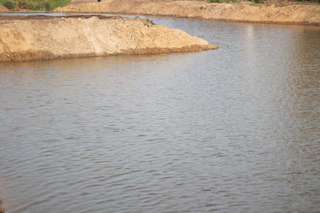 The shore of an artificial pond. A mound of sand on the water. Creation of the landscape around the lake. A sand dam on the river. Strengthening the coast. Yellow sand is abundant.の写真素材