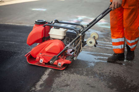 Asphalt rammer. Laying the road surface. Creation of parking. The worker levels the road surface. Hot asphalt under the pressure of the rammer.の写真素材