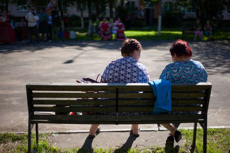 Elderly people are sitting on a bench. Old women rest in the street in the summer. Recreation place for pensioners. Two women are talking.の写真素材