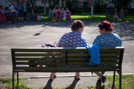 Elderly people are sitting on a bench. Old women rest in the street in the summer. Recreation place for pensioners. Two women are talking.の写真素材