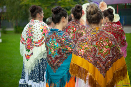 Folk scarves on the girls' shoulders. Russian traditional dress for women. Girls in the summer outdoors in beautiful clothes. The folk dance ensemble is expecting a performance.の写真素材