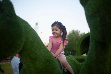 The girl sits astride a horse. Play on the playground. Asian child in the city. Child for a walk. Girl on the street.の写真素材