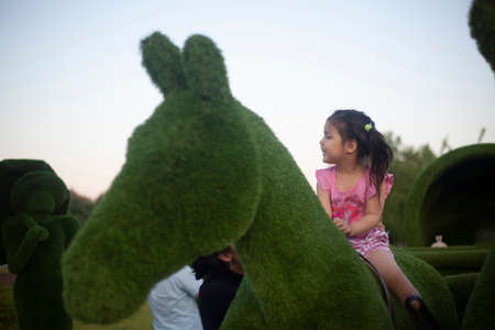 The girl sits astride a horse. Play on the playground. Asian child in the city. Child for a walk. Girl on the street.の写真素材