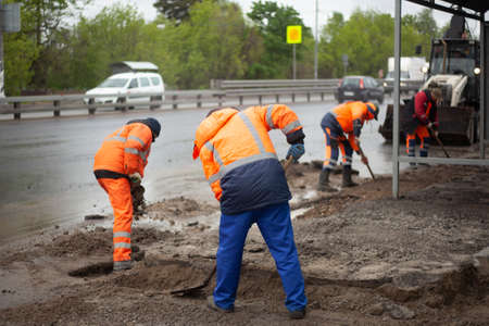 A worker with a shovel removes dirt. Renovation work. Creation of a bus stop. Replacement of road barriers. Road workers are working.の写真素材