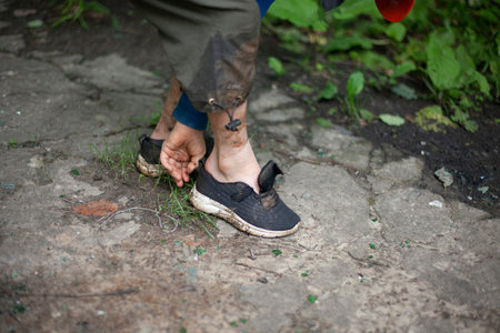 The child puts on wet and dirty shoes. The boy got his shoes dirty. The sneakers are wet....
