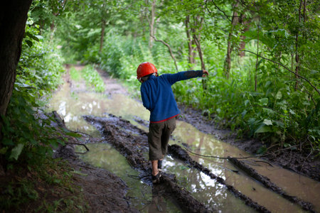 Child's Boy stands by a large puddle in the park. A child in a construction helmet. Lost son. The...