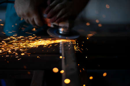 Grinding metal with a grinder. Working in a metal processing workshop. Cleaning the steel seam. The man works with an electric tool. Sparks from metal heating.の写真素材