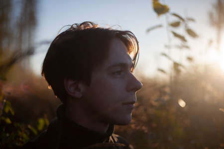 Portrait of a guy in the forest. The face of a young man on the streets. Short-haired male. The guy in the sunshine.の写真素材