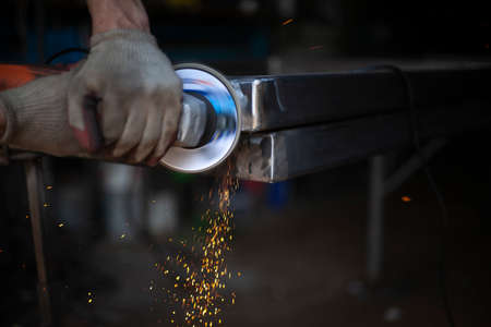 Grinding metal with a grinder. Working in a metal processing workshop. Cleaning the steel seam. The man works with an electric tool. Sparks from metal heating.の写真素材