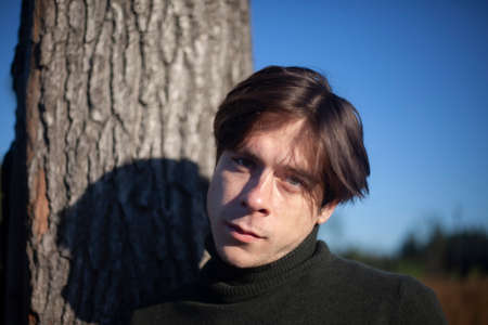 Portrait of a guy in the forest. The face of a young man on the streets. Short-haired male. The guy in the sunshine.の写真素材