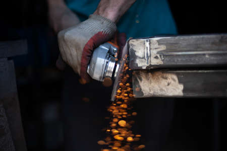 Grinding metal with a grinder. Working in a metal processing workshop. Cleaning the steel seam. The man works with an electric tool. Sparks from metal heating.の写真素材