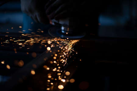 Grinding metal with a grinder. Working in a metal processing workshop. Cleaning the steel seam. The man works with an electric tool. Sparks from metal heating.の写真素材
