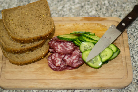 A sausage sandwich. Breakfast with bread and cucumber. Sausage sliced on a board. Simple food made from ingredients.の写真素材