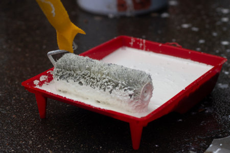 Roller in white paint. A painter applies paint to a roller with a handle. Surface painting tool.